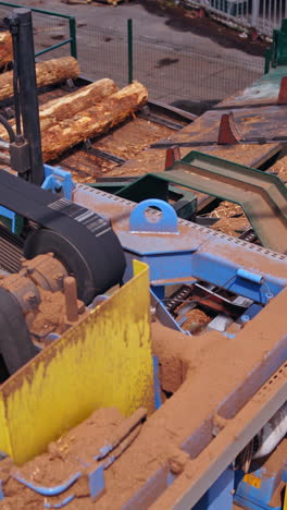 sawmill. process of removing bark from logs. special machinery with conveyor. heavy technic at plant, logging industry. view from the top. vertical video