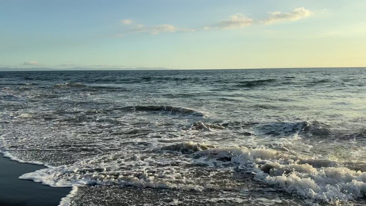Rustige oceaangolven die breken op een donker zandstrand bij zonsondergang