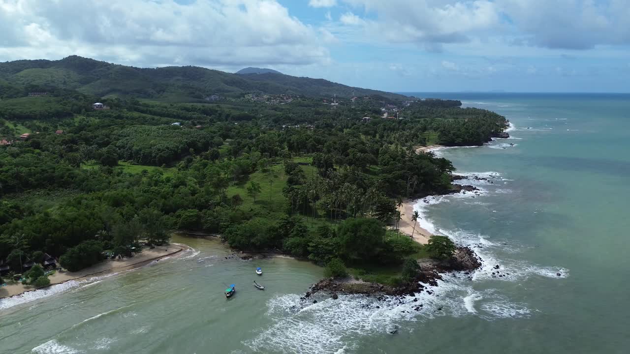Aerial drone Aerial drone footage of Koh Lanta, Thailand, featuring traditional longtail boats anchored near a tropical coastline with palm trees, rocky shore and remote beaches in the background