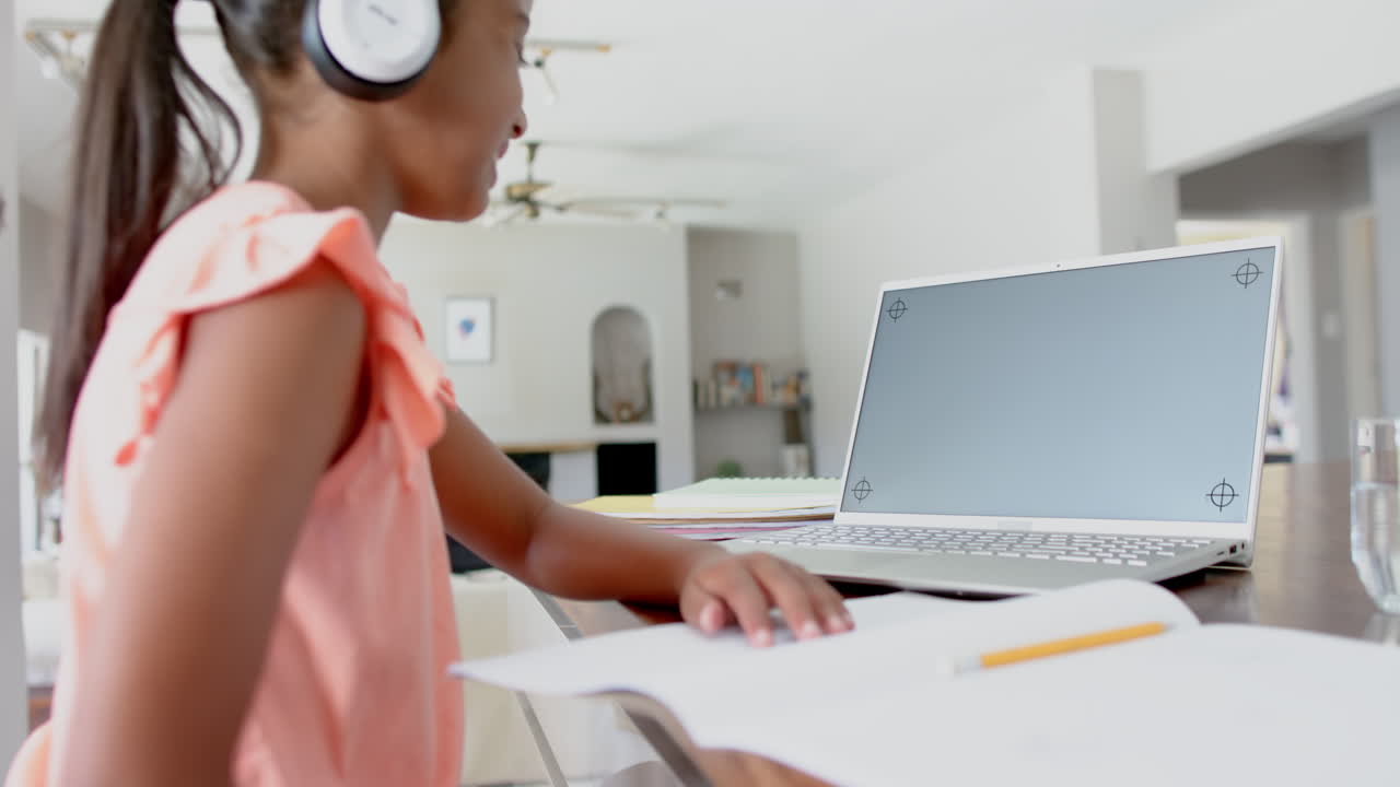 Happy biracial girl in headphones having school class on laptop, copy space on screen, slow motion