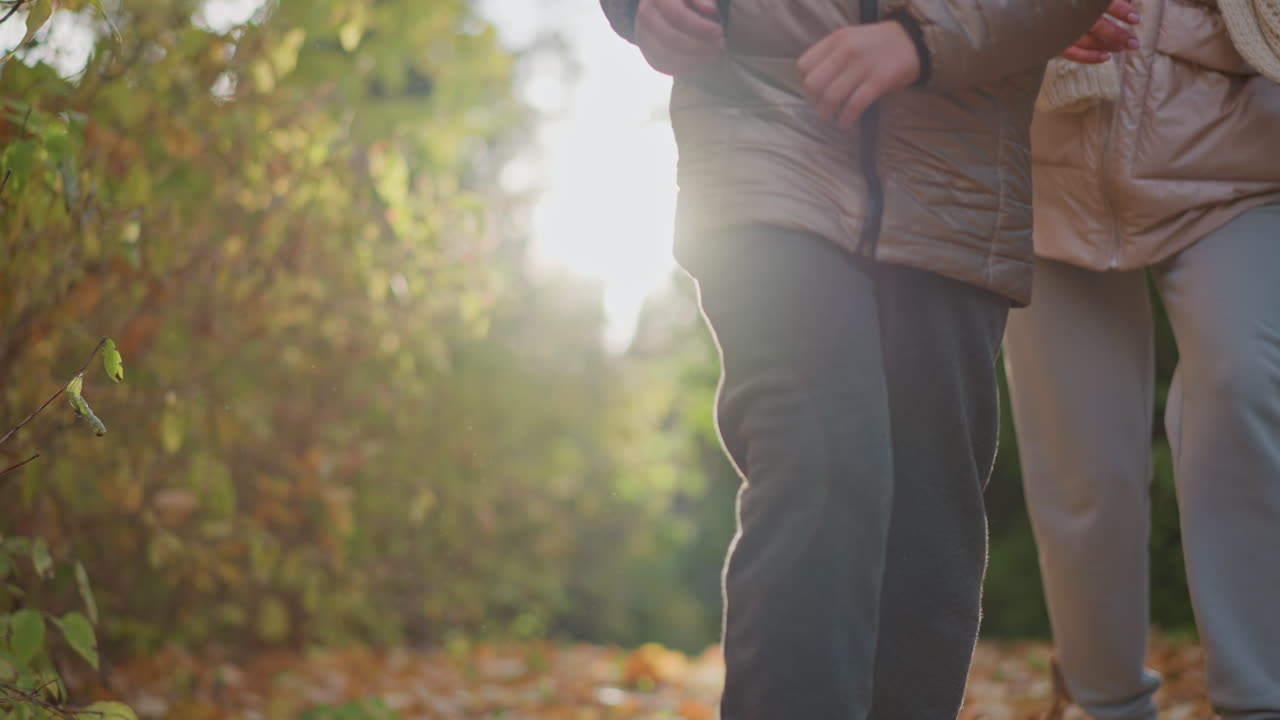 mother following daughter along sunlit forest path as child runs joyfully with golden glow around head, autumn leaves framing trail, family bond