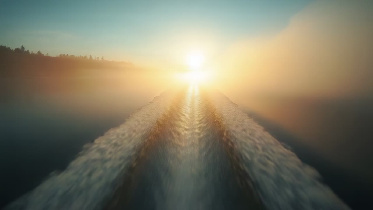 Engine propelling vessel creating central boat wake heading toward low sun on lake, revealing mist