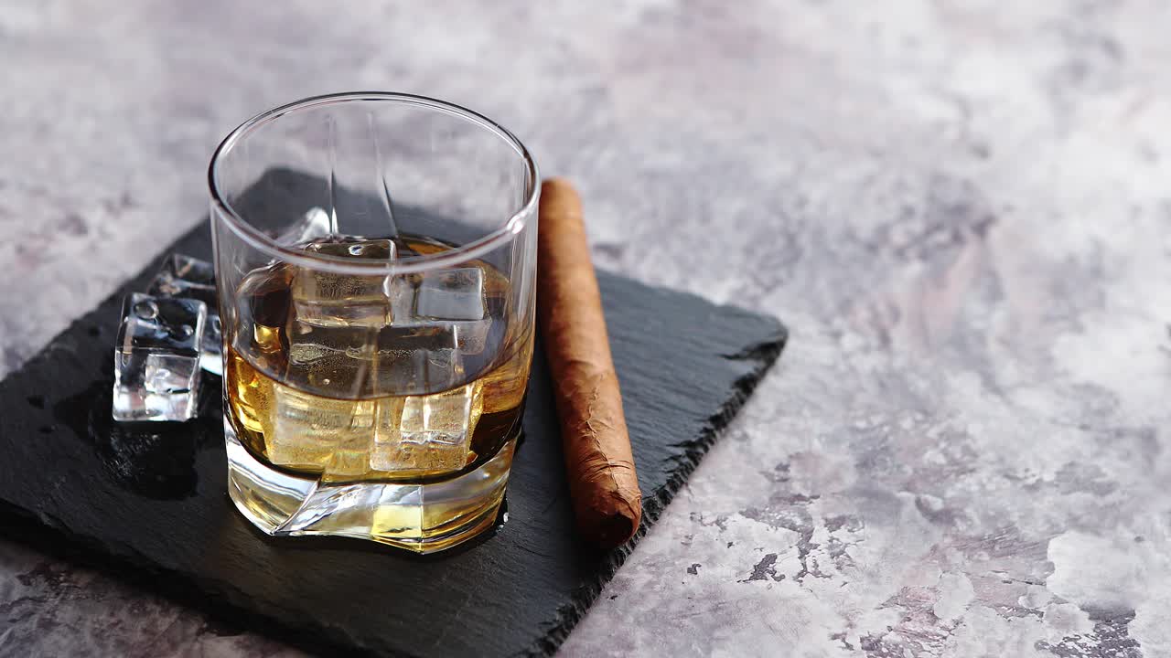 vaso de whisky con cubitos de hielo y cigarro