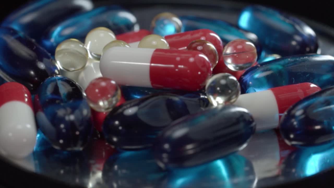Close up of assorted red, white and blue capsules with transparent softgel pills on reflective surface