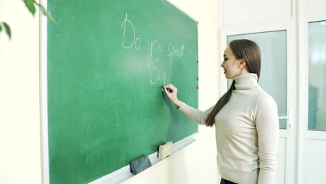 young girl at school writes in chalk on a green blackboard