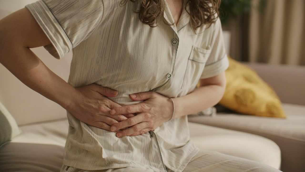 Donna che soffre di dolore addominale mentre è seduta sul divano.
