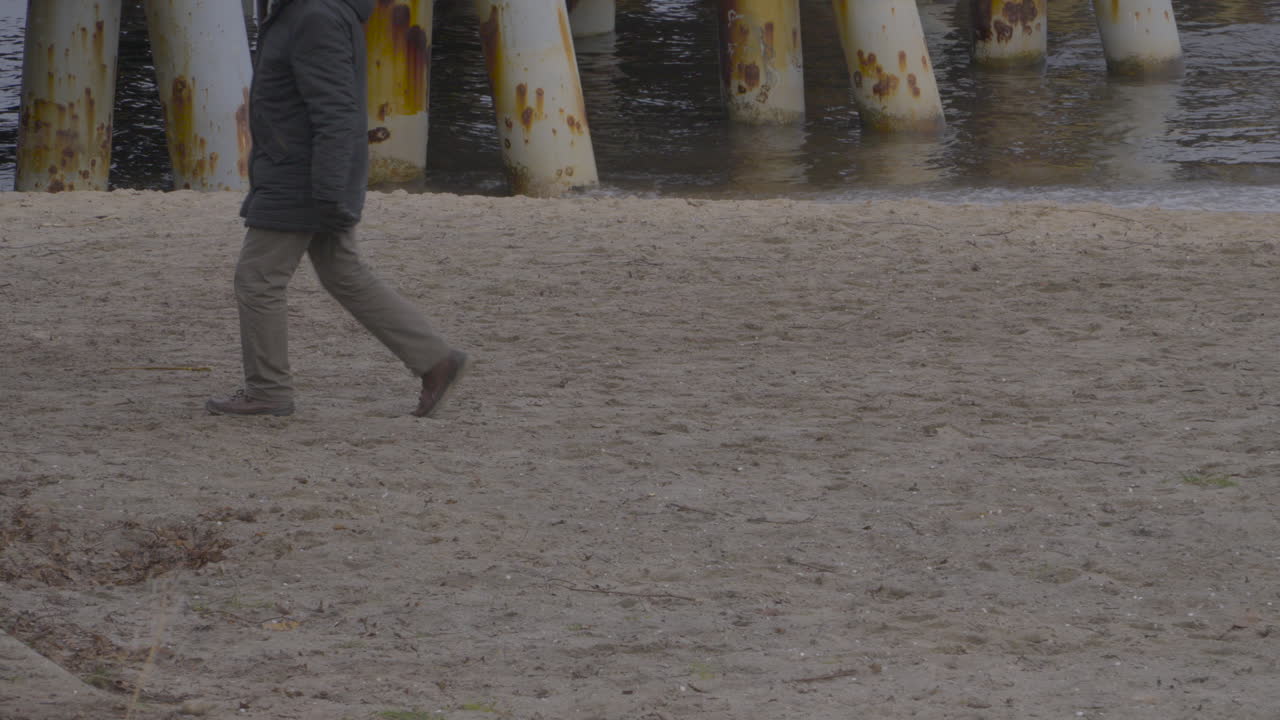 мужчина в куртке и перчатках гуляет по берегу моря