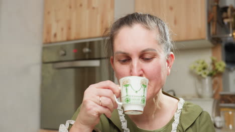 young lady in green dress enjoys quiet morning sipping hot coffee from vintage cup in cozy kitchen setting with soft lighting and wooden cabinets