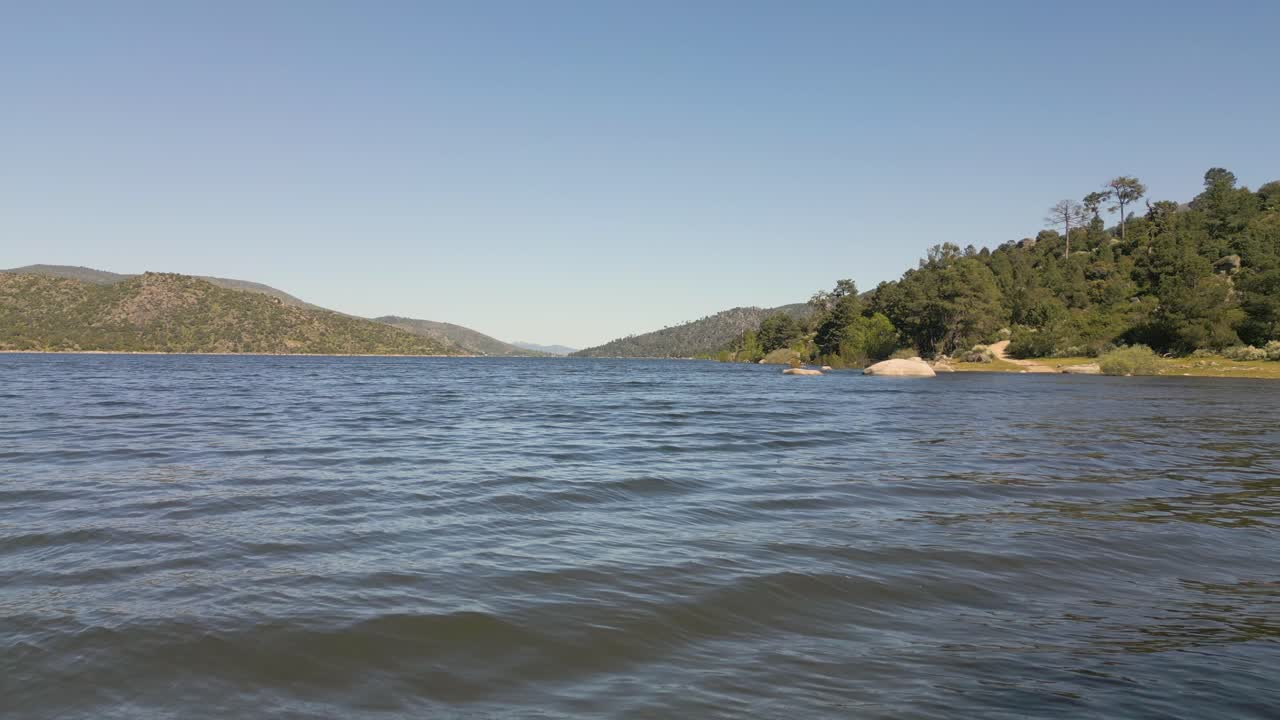 High-speed reverse drone flight over a full reservoir, passing close to partially submerged trees, including a poplar and willows. The water level is at its maximum, creating a dynamic visual effect.