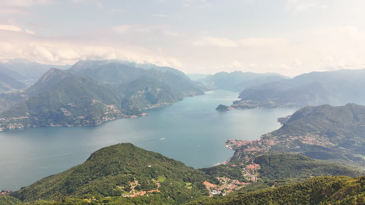 Cima Monte Grona Expansive view of Lake Comos blue waters surrounded by lush mountains and charming Italian villages under a bright summer sky, showcasing the Lombardy landscape, slow drone glide