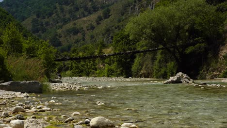 footbridge hanging over river stream, lush vegetation on high mountains in albania