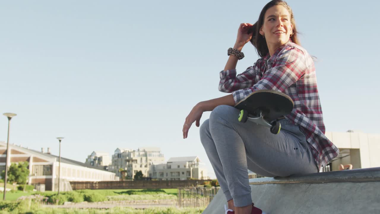 sección baja de una mujer caucásica sonriente sosteniendo un skateboard en un skatepark