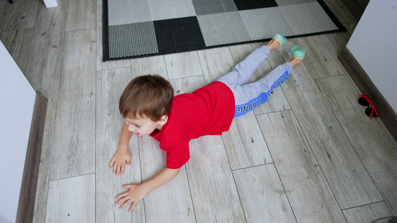 Active toddler lies on the tile floor turning around. Top view on the kid having fun at home.