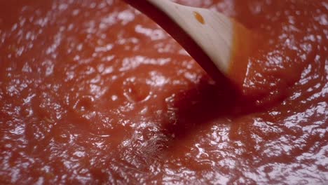 mezclando en círculo salsa de tomate roja hervida con cucharón de madera