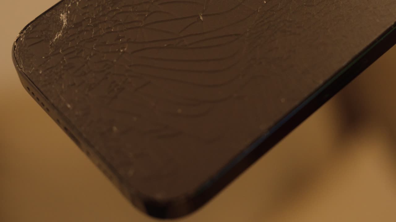 Close-up of a damaged smartphone back after falling to the floor. Cracked glass surface visible, showing realistic accident and device fragility