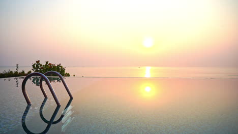 An-empty-invisible-edge-resort-swimming-pool-looks-out-over-a-pink-and-yellow-ocean-sunset