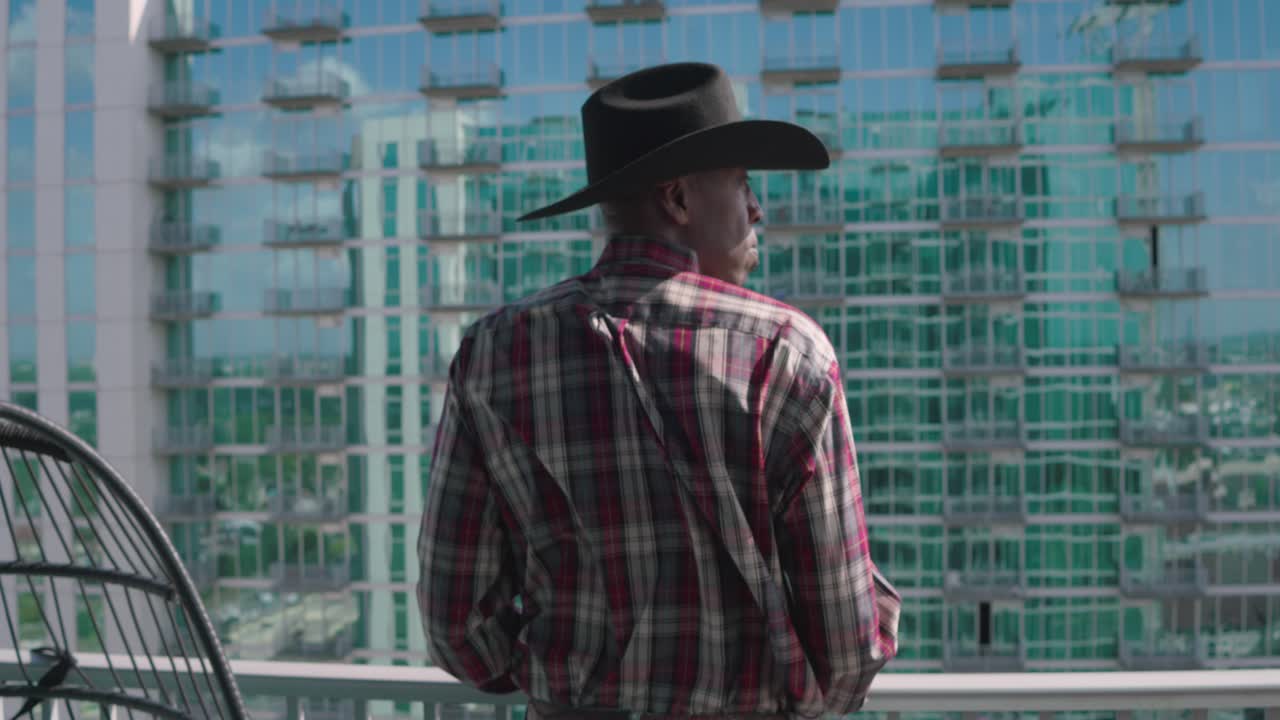 hombre negro con sombrero de vaquero negro mirando desde el balcón