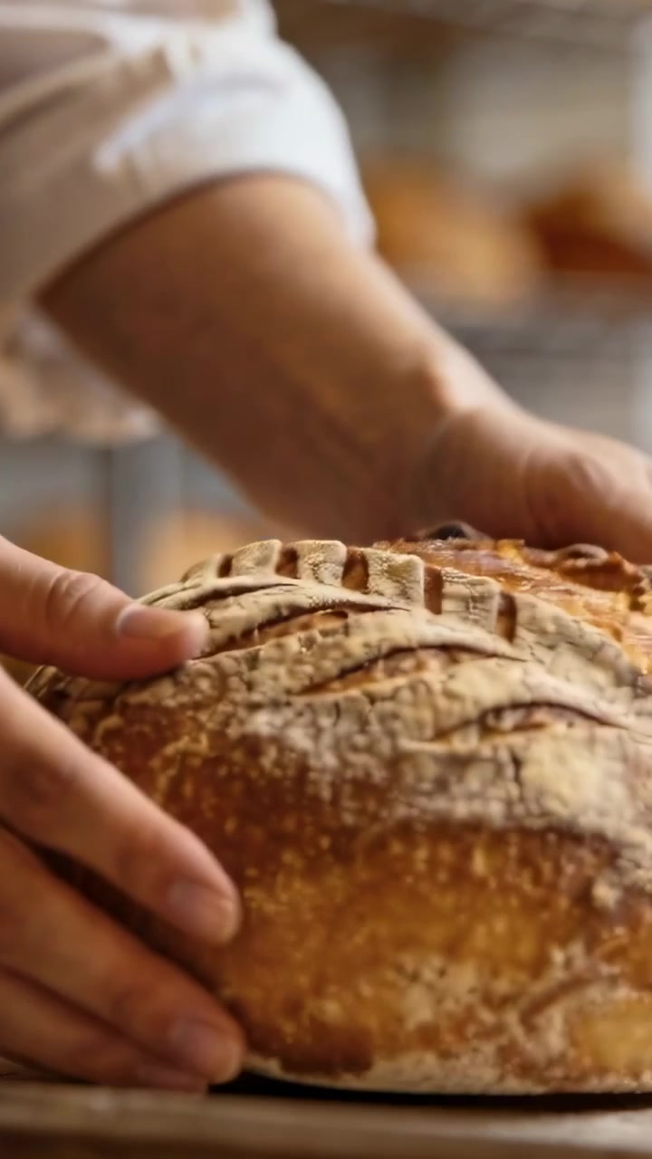 Vertical video: Lifting baker hands turning loaf after baking at bakery showing scored crust base