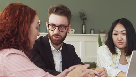 gruppe von drei multiethnischen kollegen, die am tisch sitzen und über die arbeit diskutieren 1