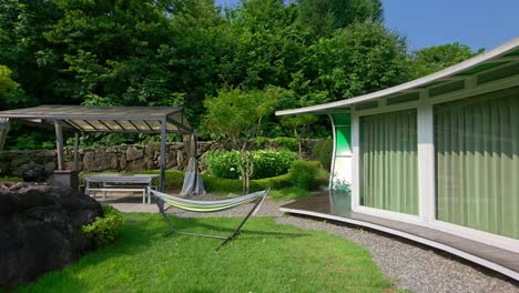 a first-person point-of-view shot walks through the beautiful garden of a luxury glamping resort in gapyeong, south korea, showing the modern cabin, hammock, and outdoor patio