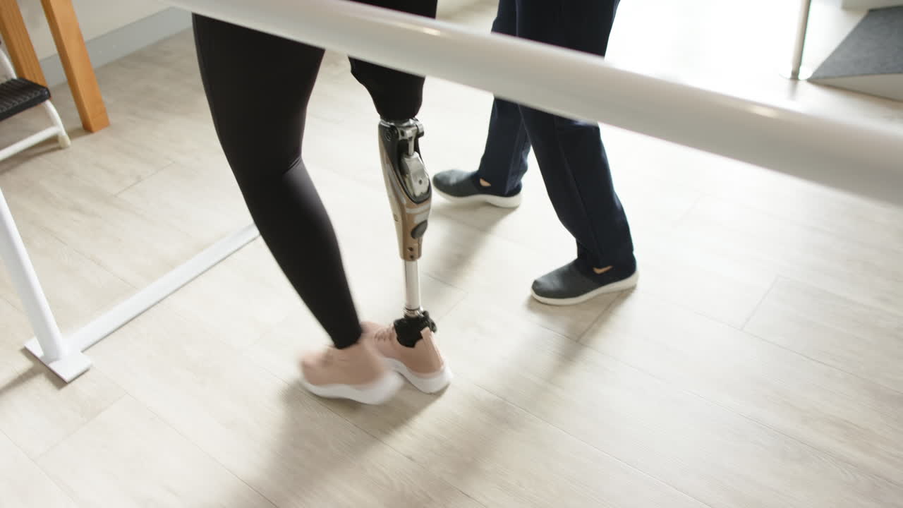 Two people standing in prosthetic lab, one with a prosthetic leg, practicing walking