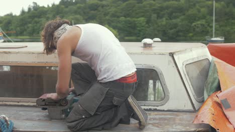 joven trabajando en topless en verano sellando el techo de la cabina del barco de madera para evitar fugas