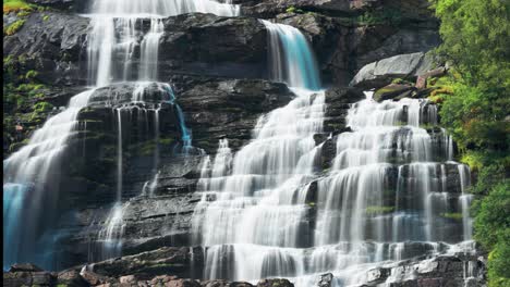 captivating footage of a waterfall tumbling down a rugged cliff, with water sparkling in the sunlight and vibrant green foliage enhancing the natural beauty