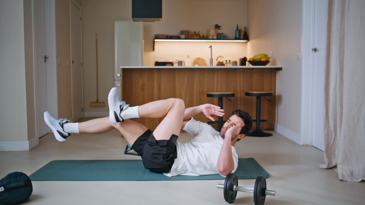 Active sportsman training abs on fitness mat home. Energetic man raising legs