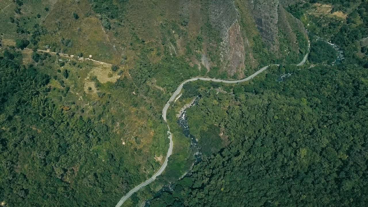 Top-down drone shot of a lone car weaving along a sinuous riverside road near Pacho, Colombia, tracing every curve through lush Andean terrain.