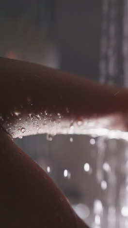 mujer bajo agua clara en la cabina de ducha de primer plano. dama con los ojos cerrados acaricia el cabello húmedo bajo aerosoles cálidos en el baño. cuidado de spa para el descanso en casa
