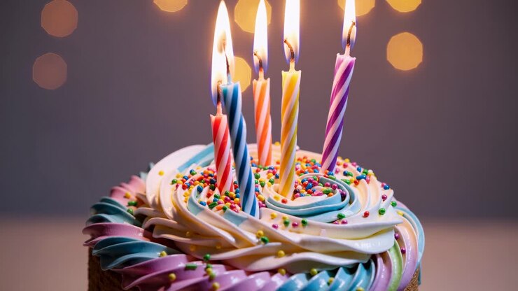Video ravvicinato di una torta di compleanno colorata con candele accese. La glassa a vortice e le luci bokeh.