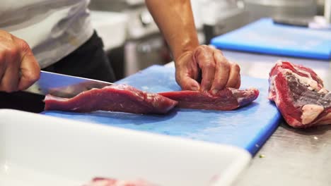 cerca de un chef cortando cuidadosamente el bistec de solomillo crudo con un cuchillo en un tablero en cámara lenta
