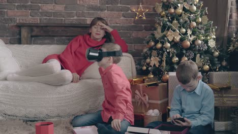 los hermanos se divierten con regalos tecnológicos de año nuevo cerca de su madre.
