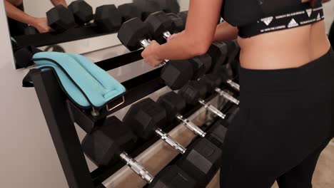 a woman chooses dumbbells from a rack in a well-lit gym, focusing on strength training. the setting is modern and organized