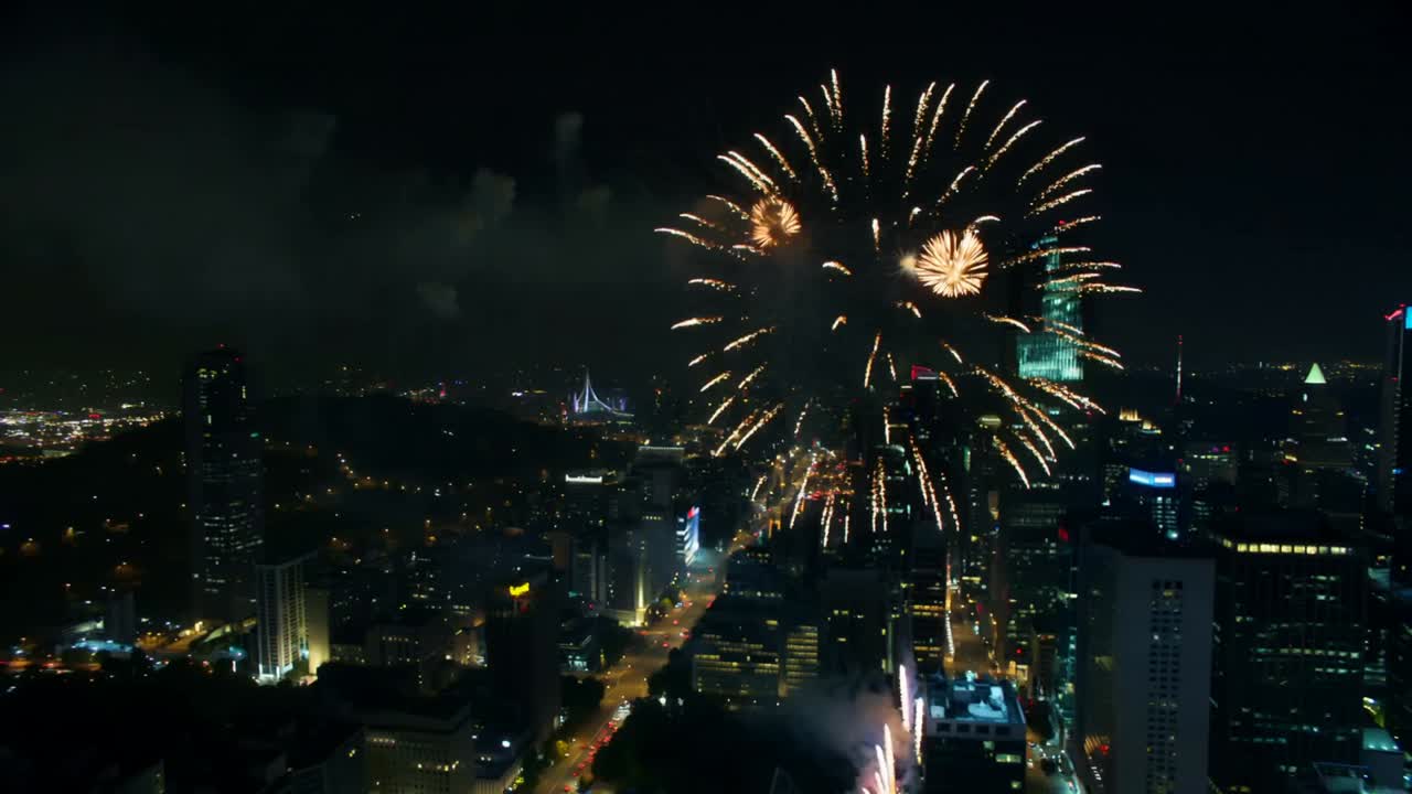 Opening aerial downtown causing fireworks shells shooting from rooftop sending smoke and bursts up