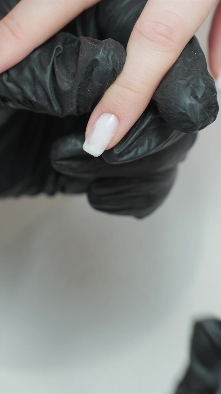 Close up view of hand wearing black gloves receiving detailed nail polish application. focus remains on nails and gloved hands emphasizing precision in manicure techniques