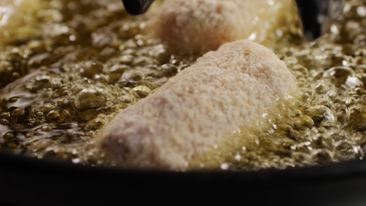 Portuguese croquettes broiling on black frying pan close-up macro. Breaded croquette of fish, potatoes and ham. Man cooking spanish food. High quality 4k footage