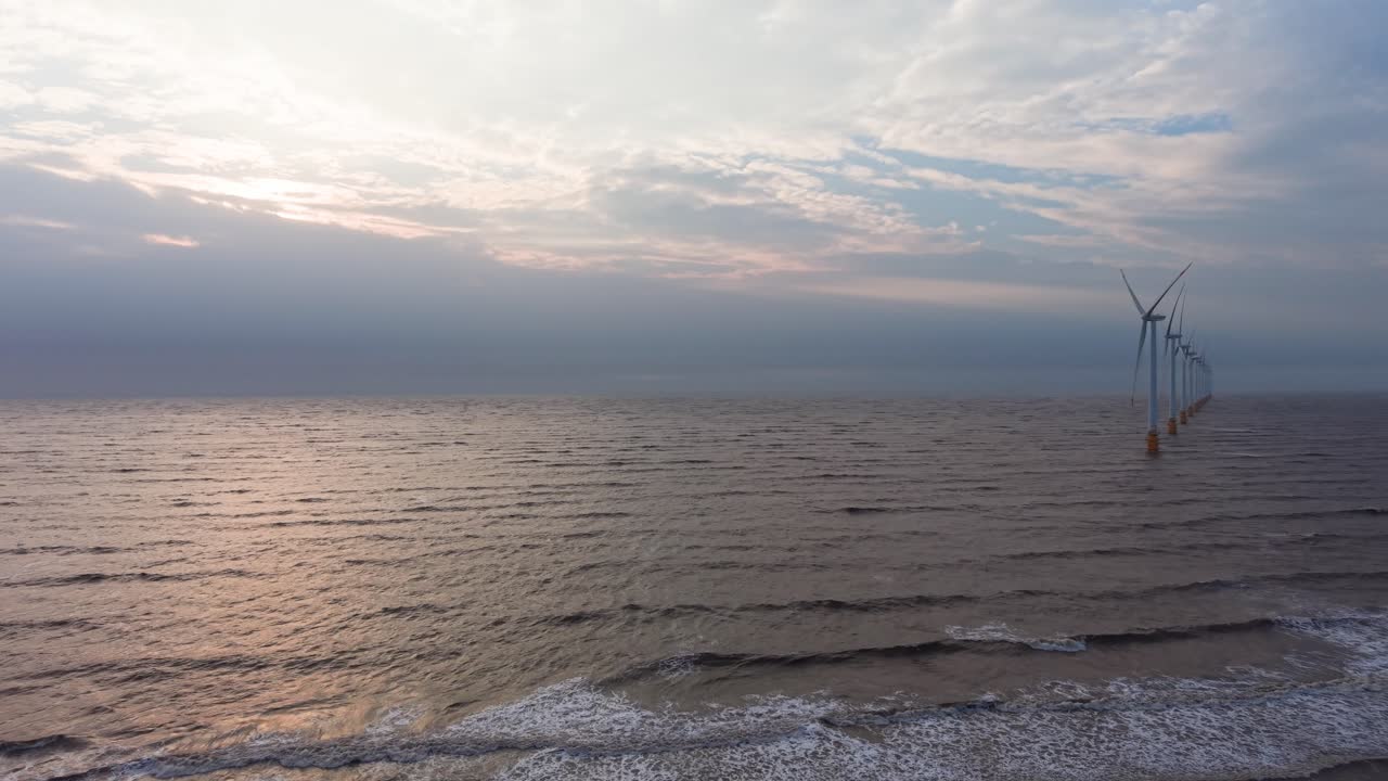Le turbine eoliche dominano la costa a Tra Vinh, Vietnam, all'alba, con onde e alberi in vista.