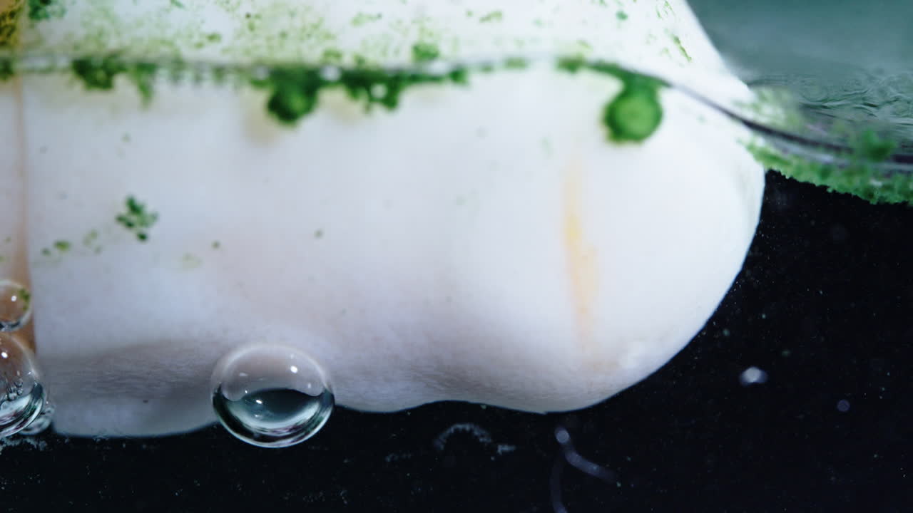 Dissolving pill in liquid with bubbles and green powder floating around