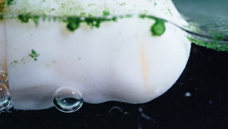dissolving pill in liquid with bubbles and green powder floating around