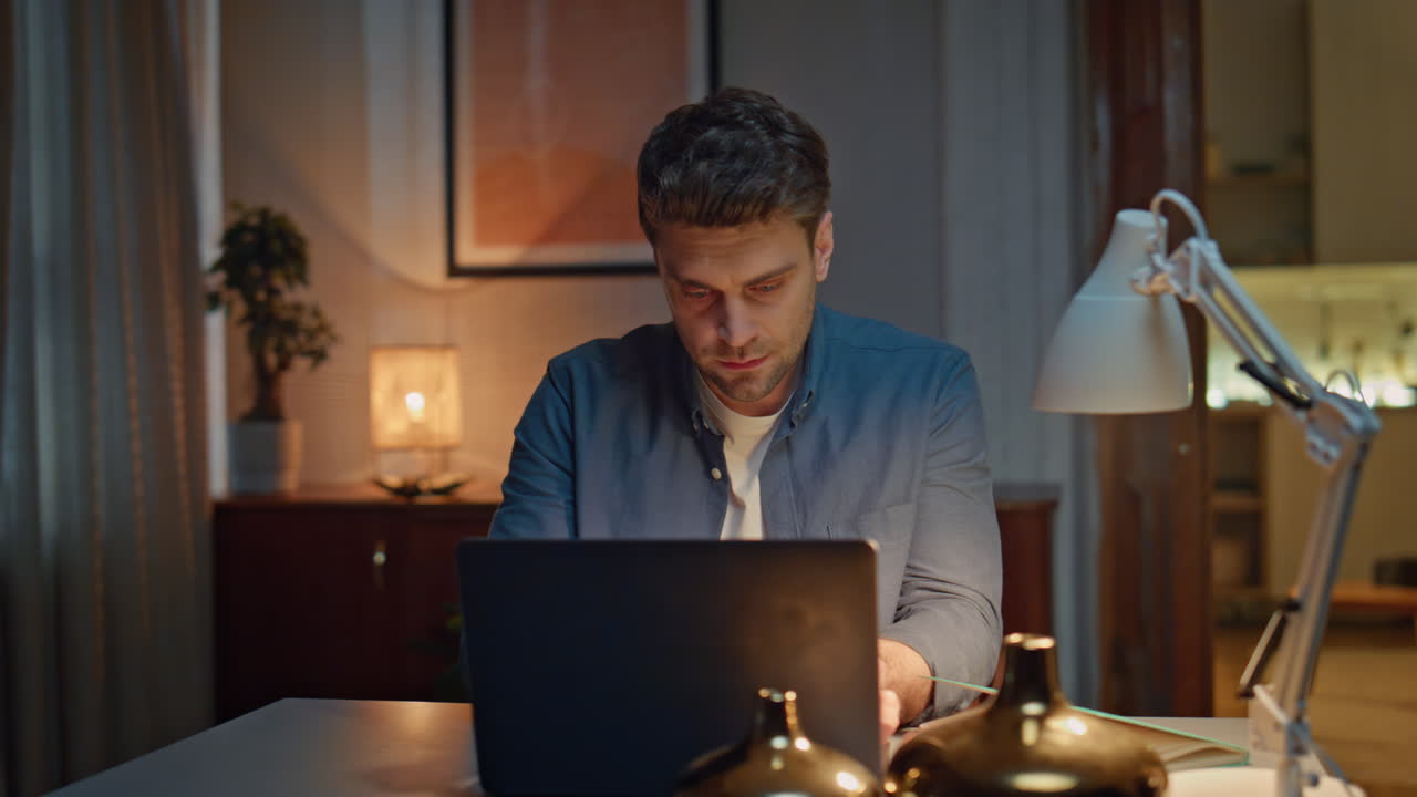 Late worker open laptop at evening flat closeup. Serious man writing notes alone