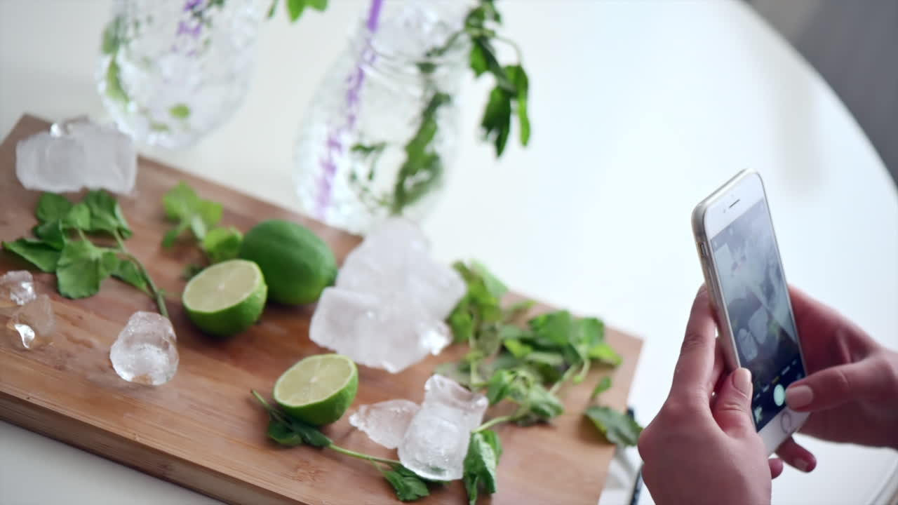 Woman taking pictures of cut up lime with ice and mint on a wooden cutting board