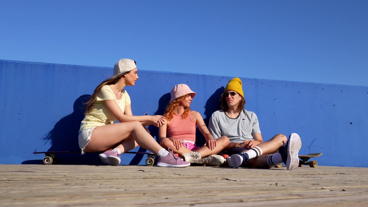 Friends relaxing with skateboards by a blue wall