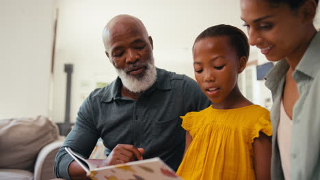 grandfather congratulating granddaughter reading book at home with mother