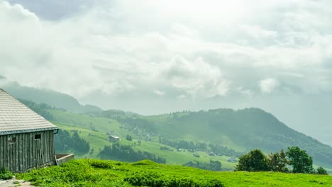 a wooden farmhouse overlooks the rolling green pastures of amden, st. gallen, switzerland, with misty mountains in the background. the timelapse captures shifting clouds and dynamic light changes.