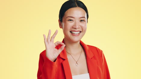 smile, ok sign and face of asian woman on yellow