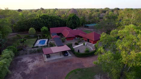 drone shots of a rural estate with a red house, pond, swimming pool, stone gardens and green lawns