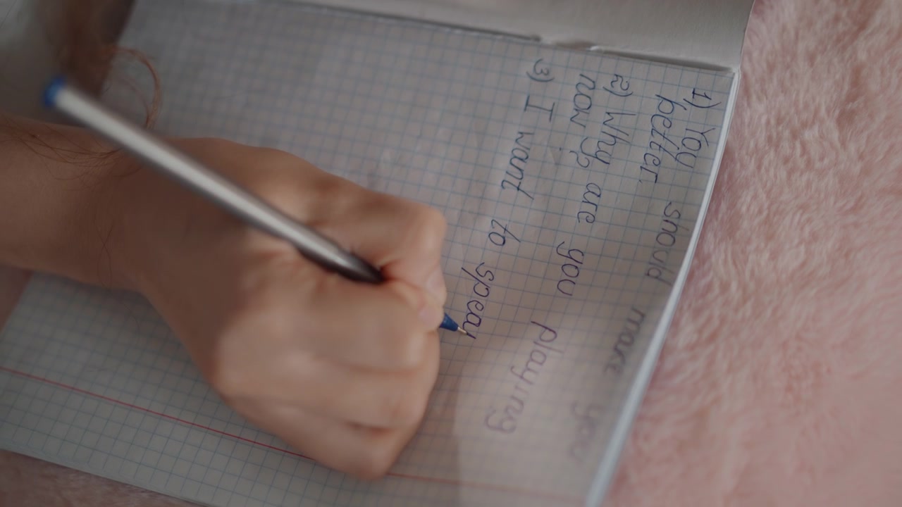 Vista próxima e angulada de uma mão escrevendo ativamente números e marcas de seleção em uma página de caderno quadriculada com caneta, mostrando notas organizadas, contagens e cálculos em um espaço de estudo focado.