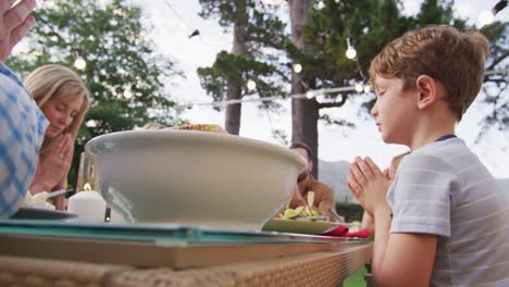 three generation family praying before having lunch outdoors