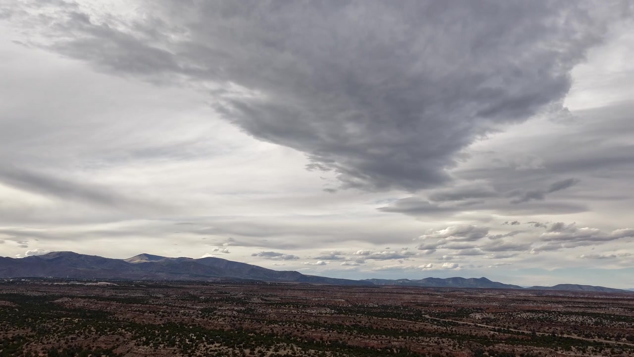 A cinematic drone timelapse captures a vast blanket of layered clouds over southwestern mesas. Distant mountains and shifting atmospheric motion create an epic and expansive nature backdrop.